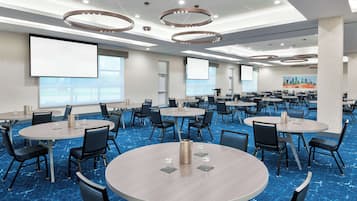 Un salón de conferencias con varias mesas, sillas y una pantalla grande.
