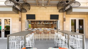 A bar area with a long counter, multiple bar stools, and a seating area with white chairs. - Hyatt House Tampa Airport Westshore (Tampa)