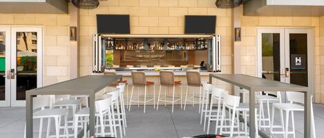 A bar area with a long counter, multiple bar stools, and a seating area with white chairs.