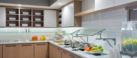 Una cocina moderna con armarios blancos, un dispensador de agua de vidrio y un frutero.