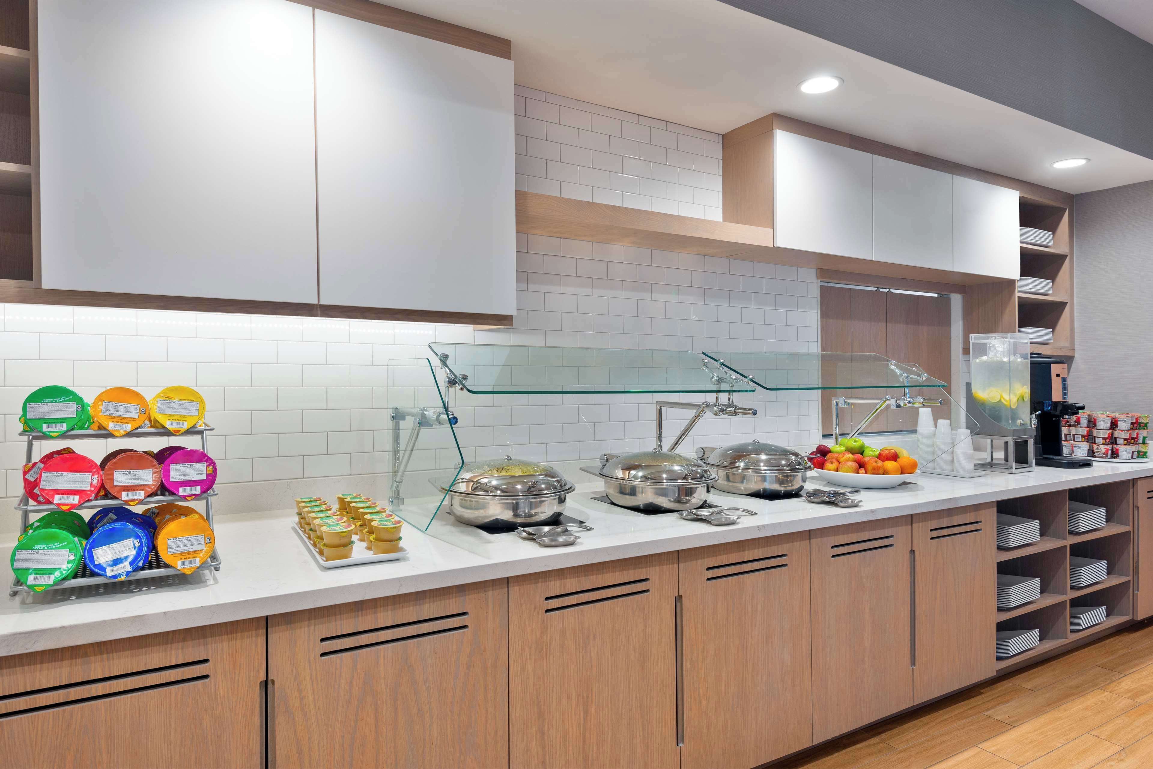 A modern kitchen with white cabinets, a glass display case, and a variety of food items.