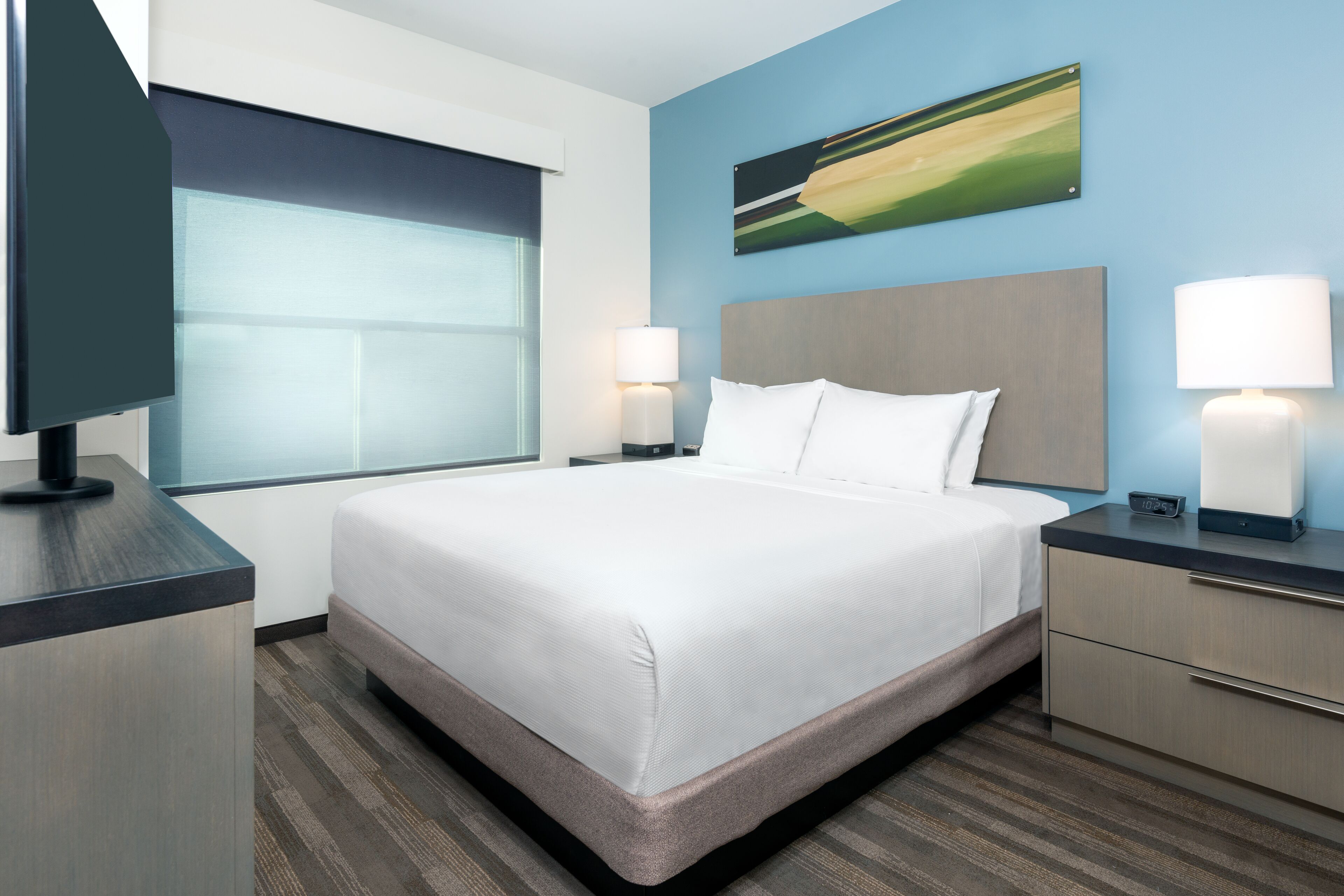 A hotel room with a large bed, two bedside lamps, a flat-screen TV, and a window with blinds.