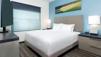 A hotel room with a large bed, two bedside lamps, a flat-screen TV, and a window with blinds.