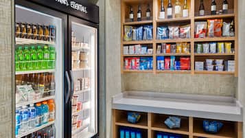 Un bancone refrigerato con diverse bevande e snack, ed scaffali pieni di bevande in bottiglia e prodotti confezionati.