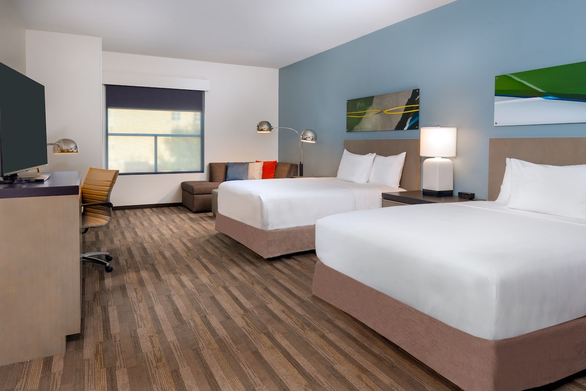 A hotel room with two beds, a desk, a chair, and a window.