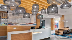 A modern reception area with a wooden reception desk, multiple seating arrangements, and hanging pendant lights. - Hyatt House Tampa Airport Westshore (Tampa)