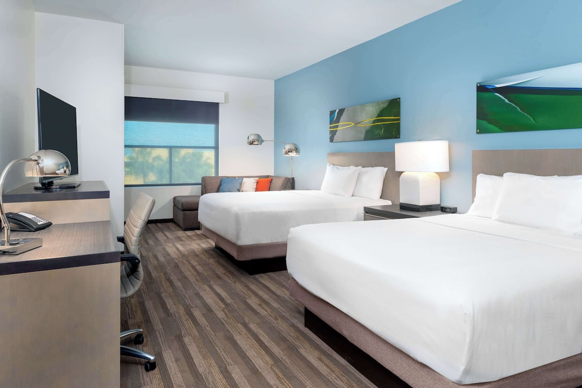 A hotel room with two beds, a desk with a computer and phone, a chair, and a window with a view.