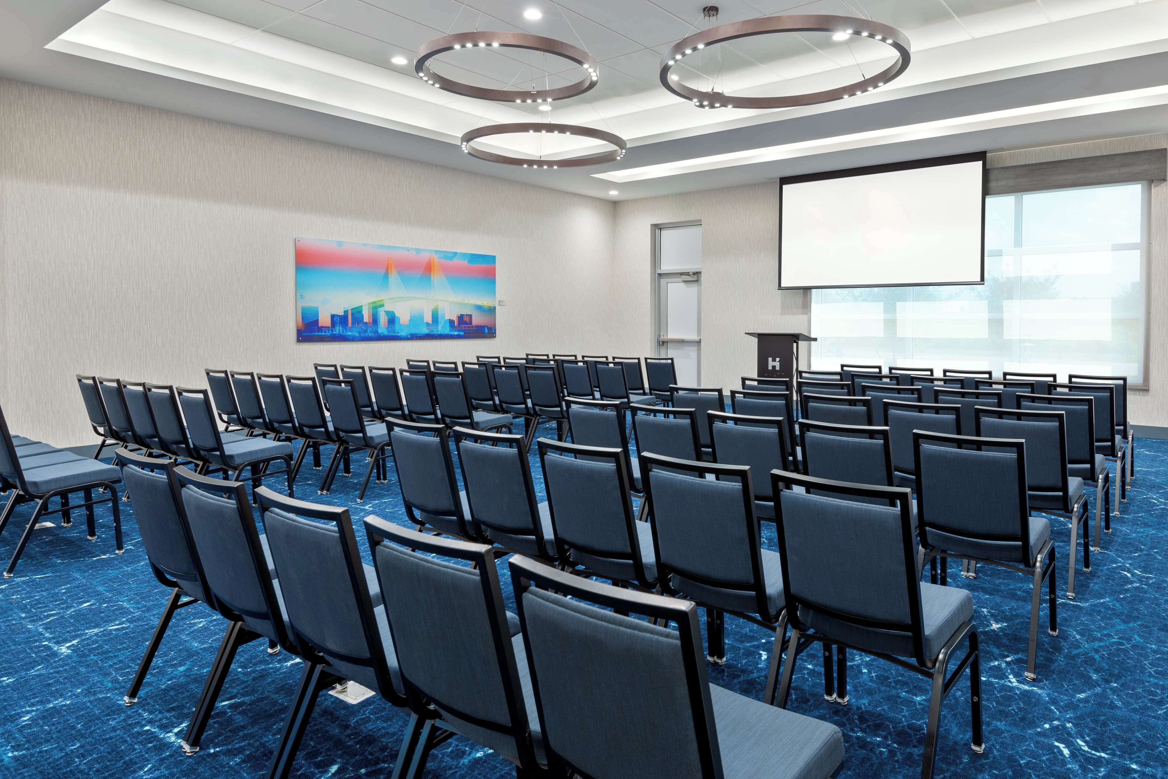A conference room with rows of chairs, a projector screen, and a presentation podium.