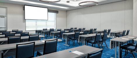 A conference room with multiple tables and chairs, a large screen, and a projector.