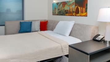 Quarto de hotel com cama, mesa de cabeceira com abajur, quadro na parede e janela com vista.