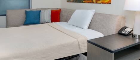 A hotel room with a bed, a bedside table with a lamp, a painting on the wall, and a window with a view.