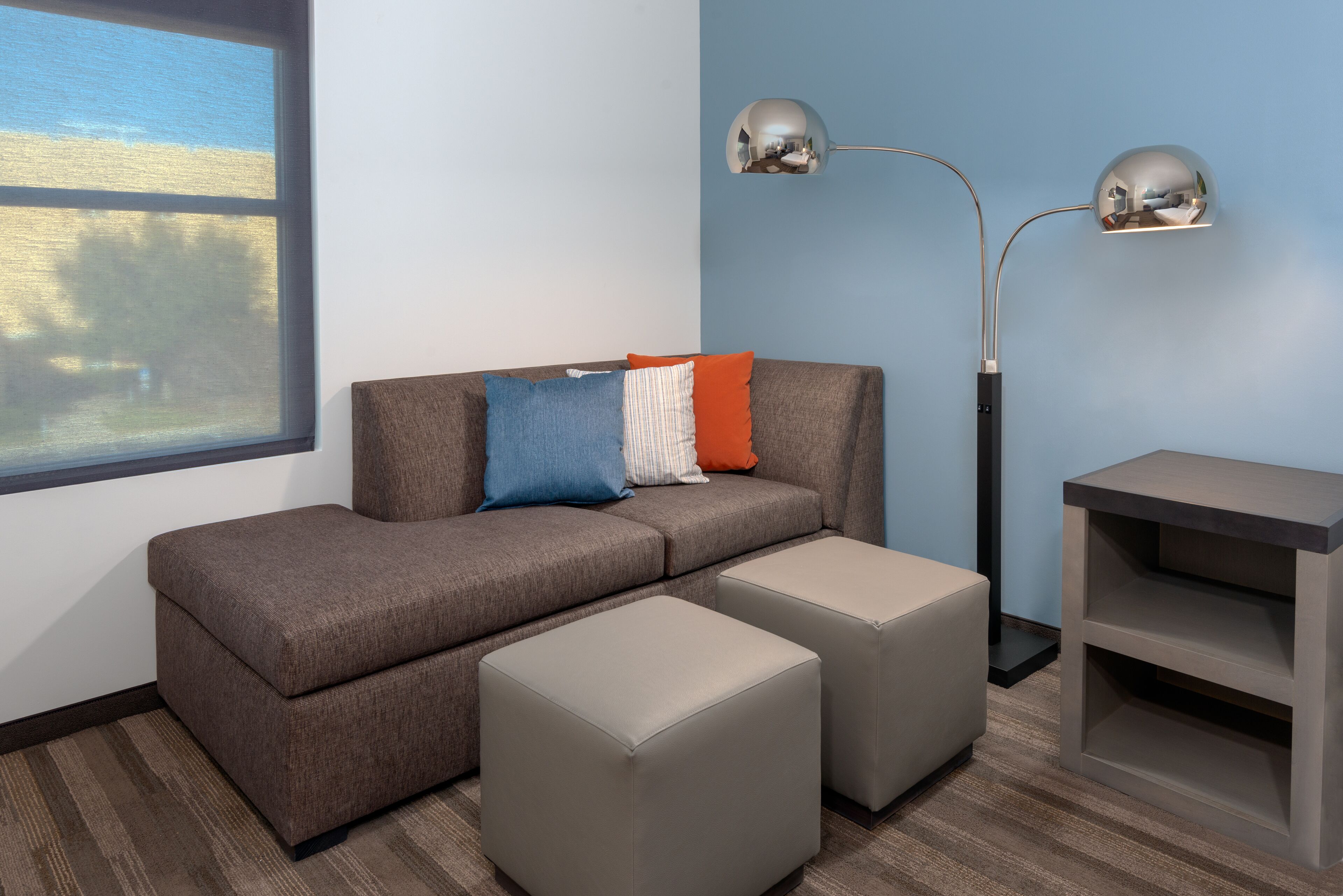 A modern living room with a sofa, ottomans, a side table, and a floor lamp.