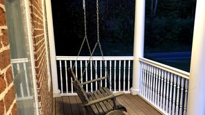 A porch with two wicker rocking chairs and a swing, white railings, and a brick wall. - Historic Vermont Farmhouse on 12 Acres, Quaint Vermont Experience. (Andover)