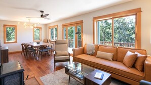 Un salon spacieux doté d’un plancher en bois, d’une grande fenêtre, d’un canapé, d’une table à manger avec des chaises et d’un ventilateur de plafond.