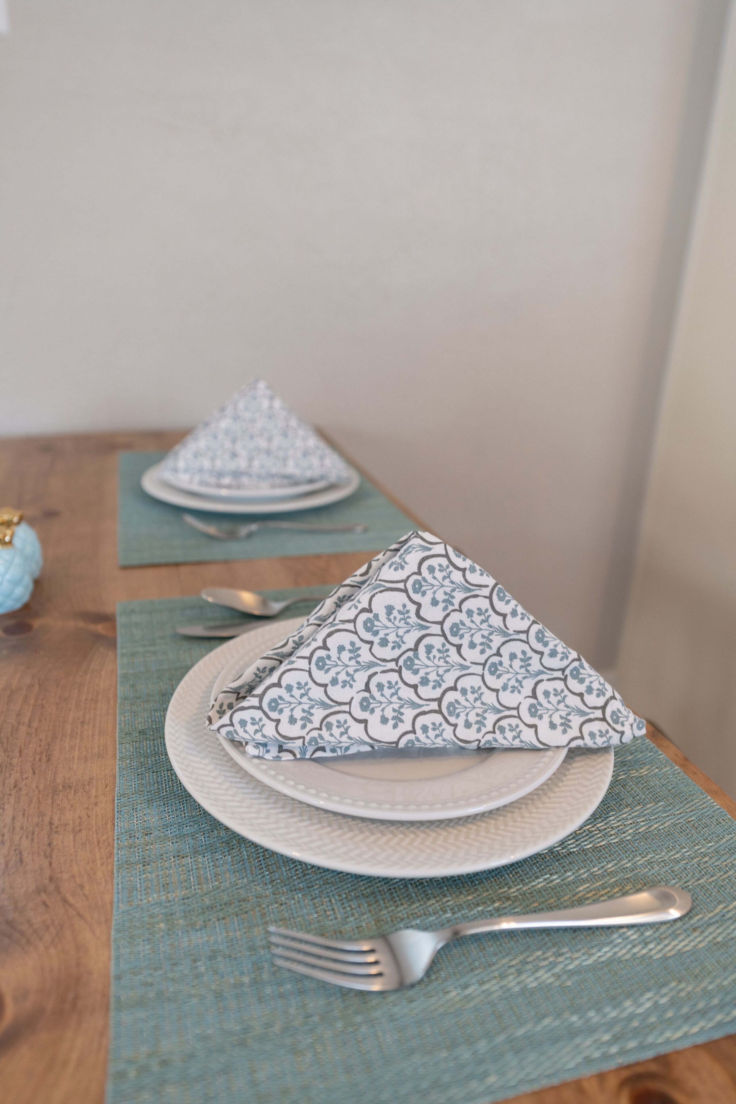 A dining table with a placemat, a folded napkin, a spoon, and a fork.