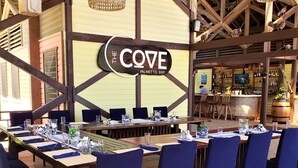 Un restaurante con una larga mesa de madera dispuesta para una comida, sillas tapizadas en azul y lámparas colgantes de mimbre.