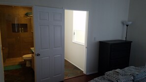 Ein Zimmer mit einer weißen Tür, einem kleinen Fenster, einem dunklen Schrank und einer Dusche.