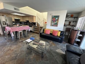 A modern kitchen with a dining area, a black leather sofa, and a staircase leading to an upper level.