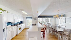 Eine moderne Küche mit weißen Schränken, einer zentralen Kochinsel und einem Essbereich mit Holztisch und Stühlen.