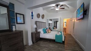 A bedroom with a bed, nightstands, a dresser, a ceiling fan, a mirror, and a TV. - Casa Sevilla, Coqui Studio (San Juan)