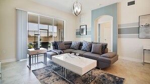 A modern living room with a sofa, coffee table, and a view to the outside. - Luxury 2BR Condo | First Floor | Balcony 169 (Kissimmee)