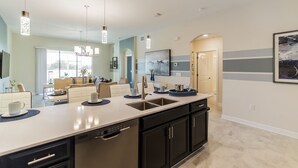 A modern kitchen with a central island, black cabinets, and pendant lighting. - Luxury 2BR Condo | First Floor | Balcony 169 (Kissimmee)