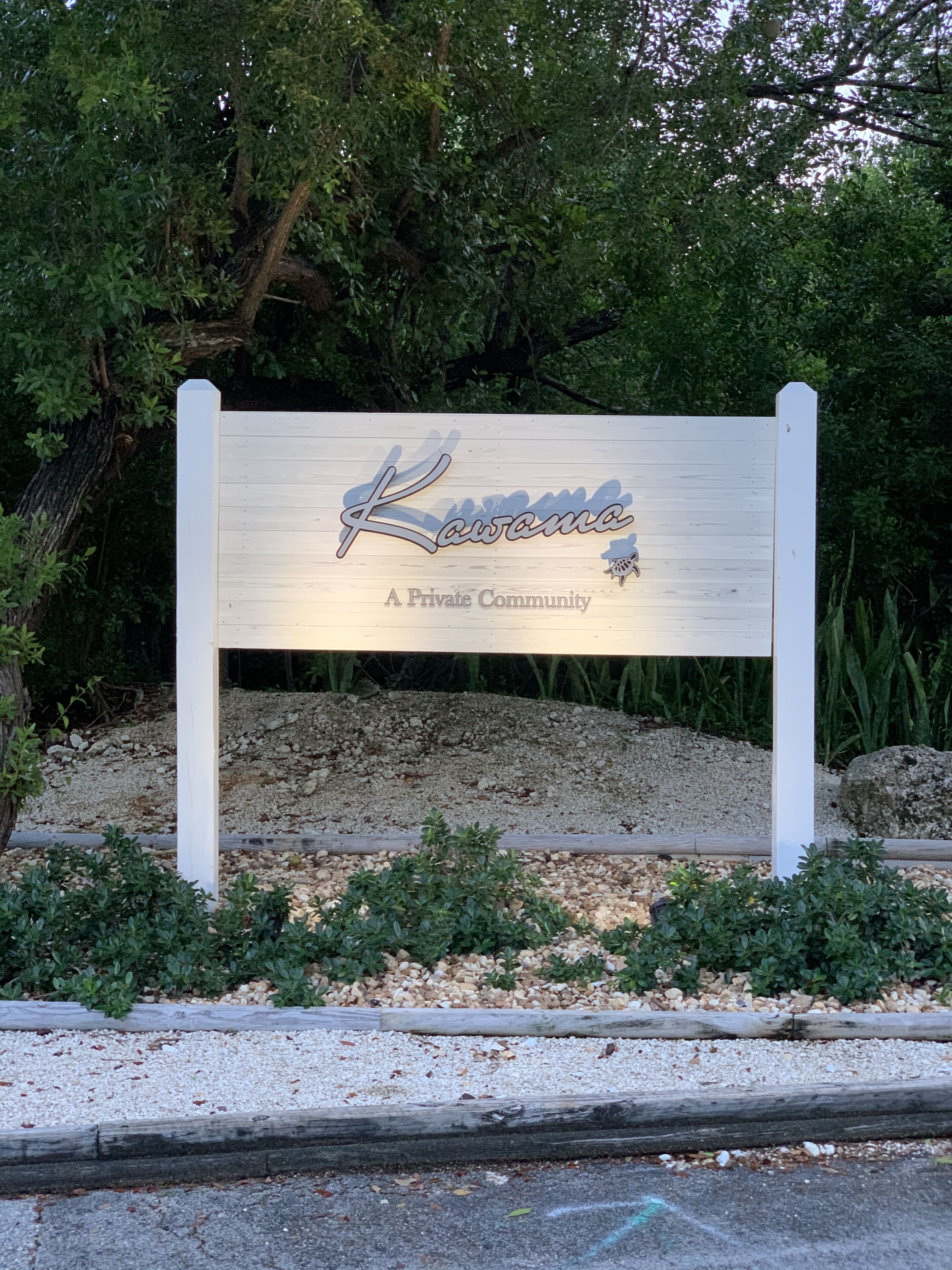 Un letrero de madera con el texto "Kawana A Private Community" rodeado de follaje y grava.