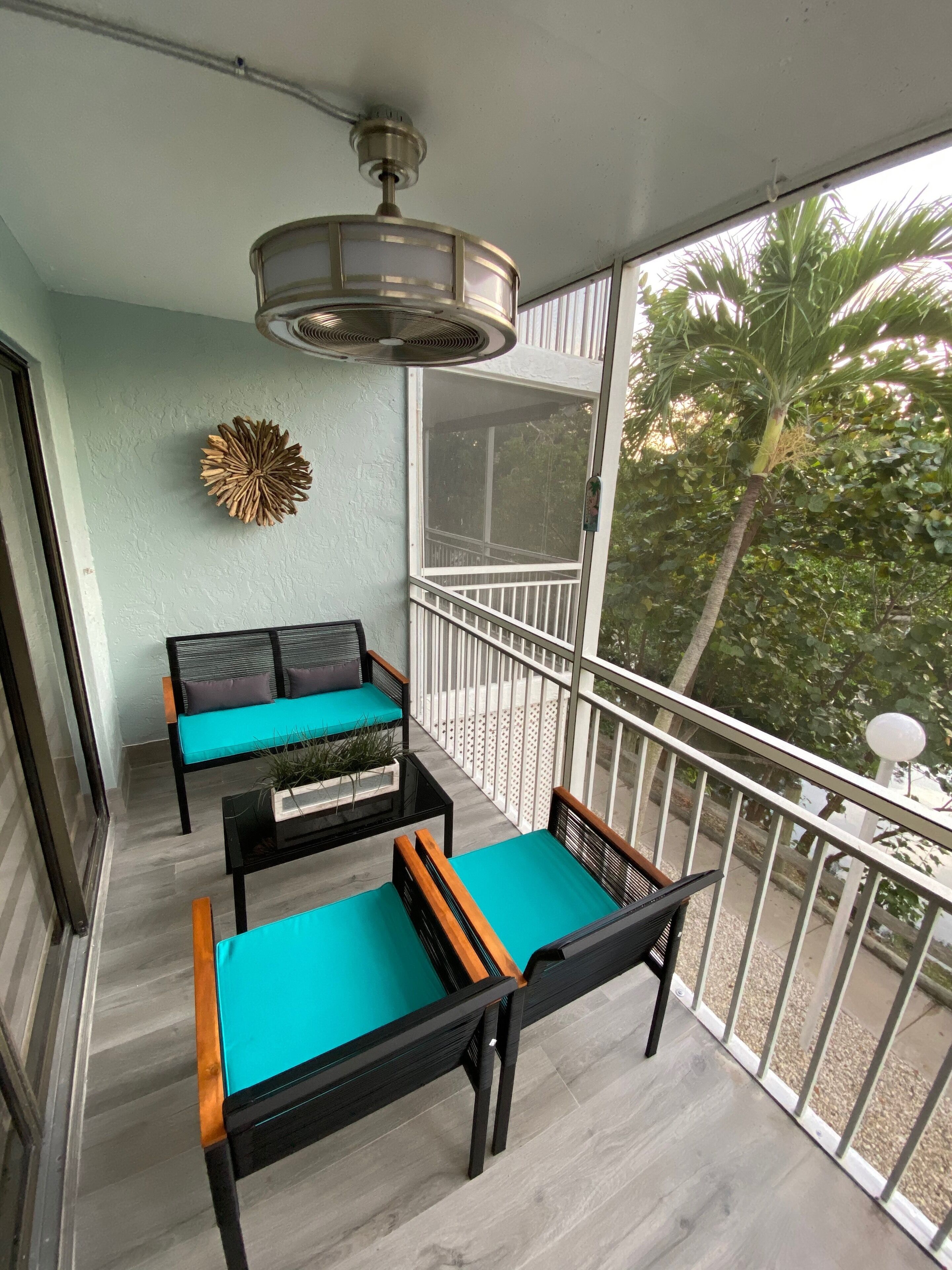 A balcony with a sofa and two chairs, a ceiling fan, and a decorative wall piece.