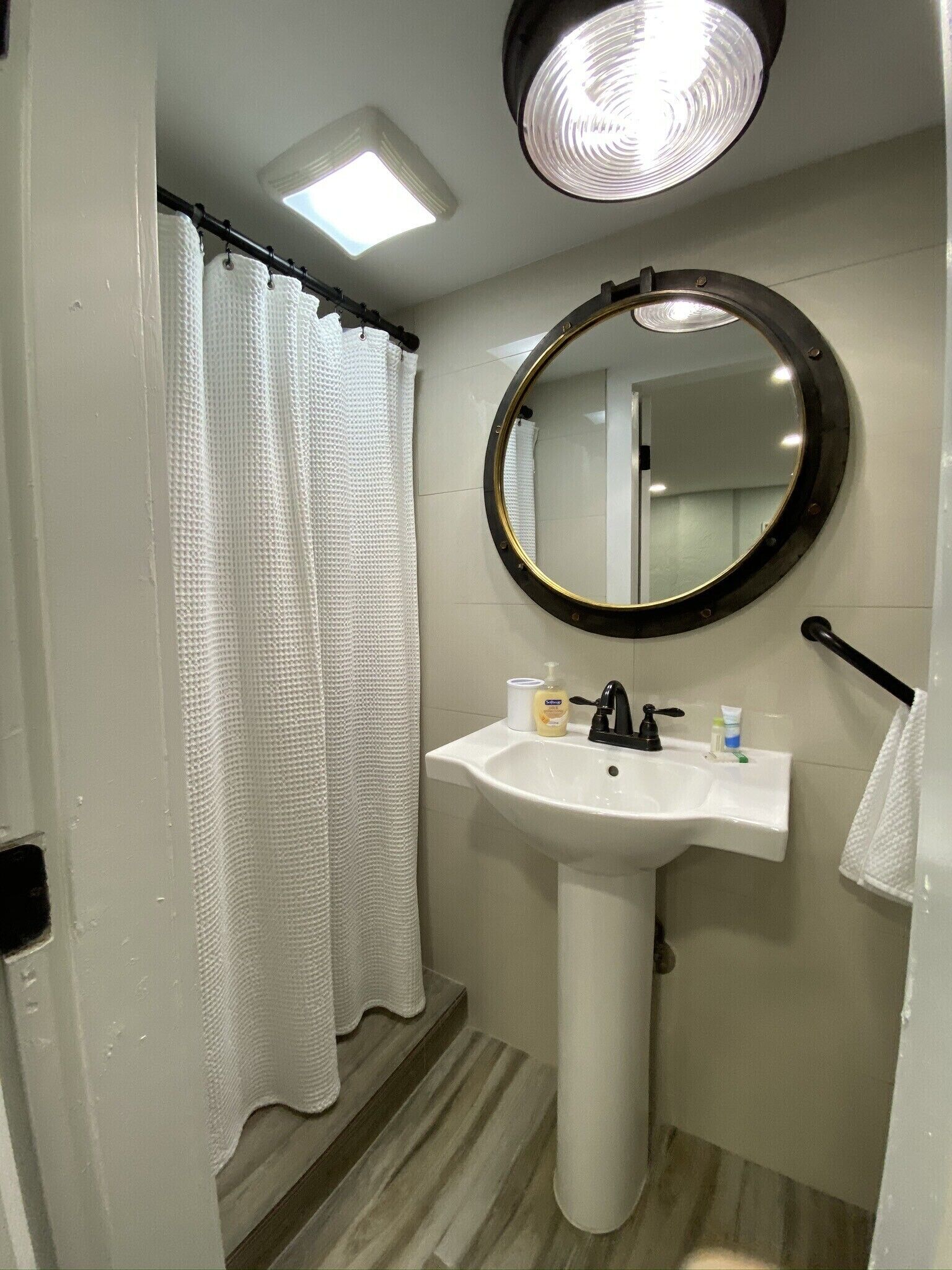 A bathroom with a white sink, a round mirror, a shower curtain, and a ceiling light.