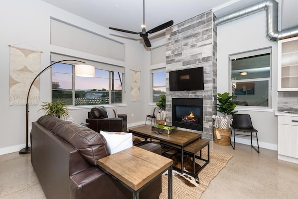 A modern living room with a fireplace, leather sofa, dining table, and large windows.