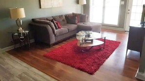 A living room with a sectional sofa, a red rug, a glass coffee table, and a lamp.