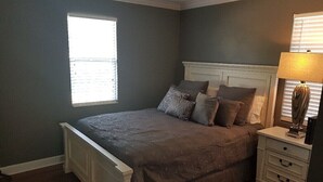 A bedroom with a bed, nightstand, lamp, and a window.