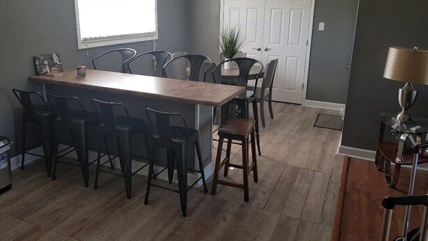 A dining area with a long wooden table, multiple chairs, a white door, and a small plant on the wall.