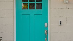 A turquoise door with a window, a doormat, and a wall-mounted light fixture. - Serene Guest House - Foodie Oasis - Walk to Folk, Audrey, Red-Headed Stranger! (Nashville)