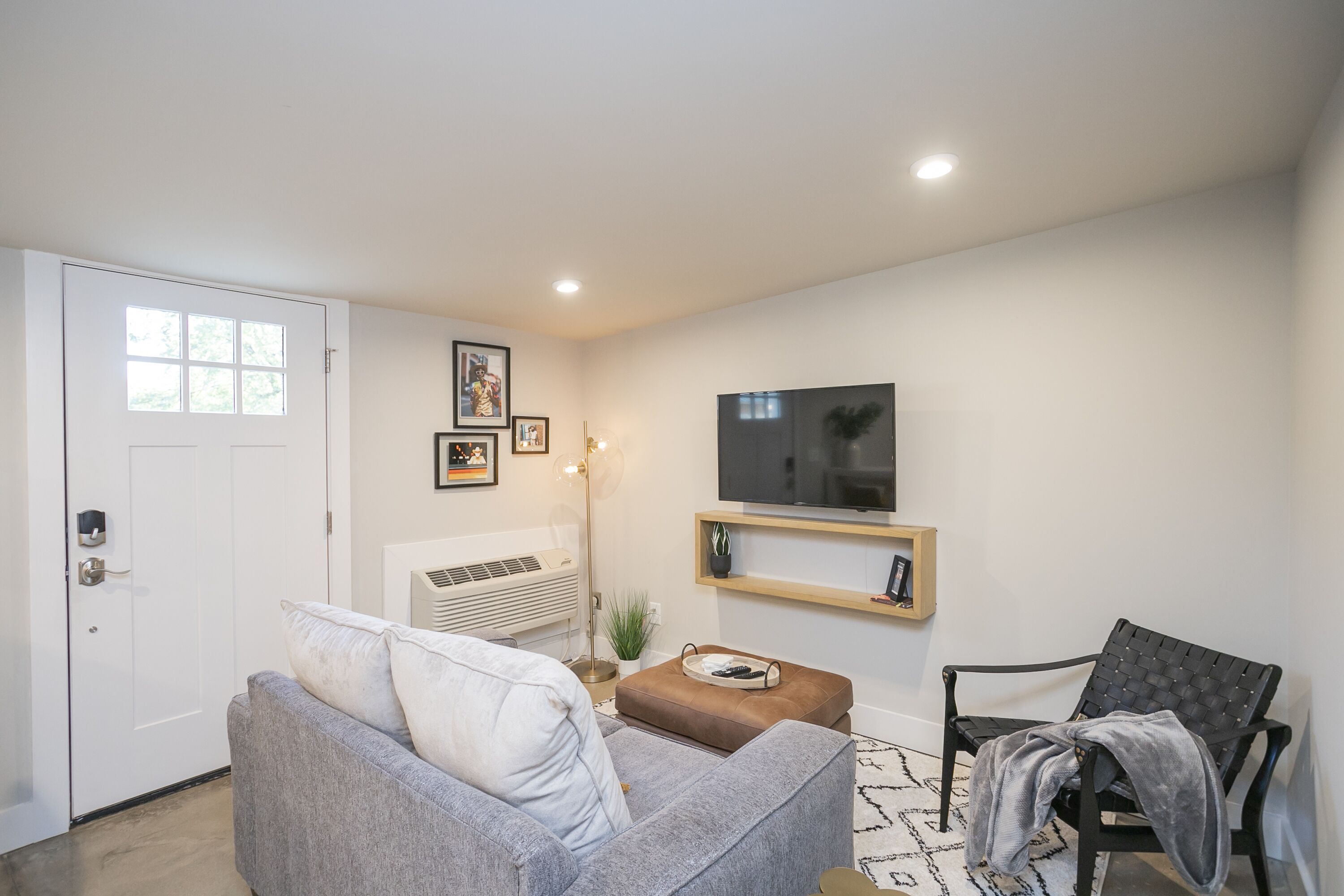 Una sala de estar con un sofá gris, un sillón negro, un televisor de pantalla plana y una mesita con una planta.