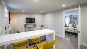 A modern living room with a white sofa, yellow chairs, a flat-screen TV, and a dining table. - Serene Guest House - Foodie Oasis - Walk to Folk, Audrey, Red-Headed Stranger! (Nashville)