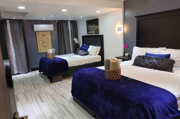 A hotel room with two beds, a large window with curtains, a wall-mounted air conditioner, and a decorative sign. - Villas Beach House(next to the main Blvd. walking distance to the beach & A/C) (Rosarito)