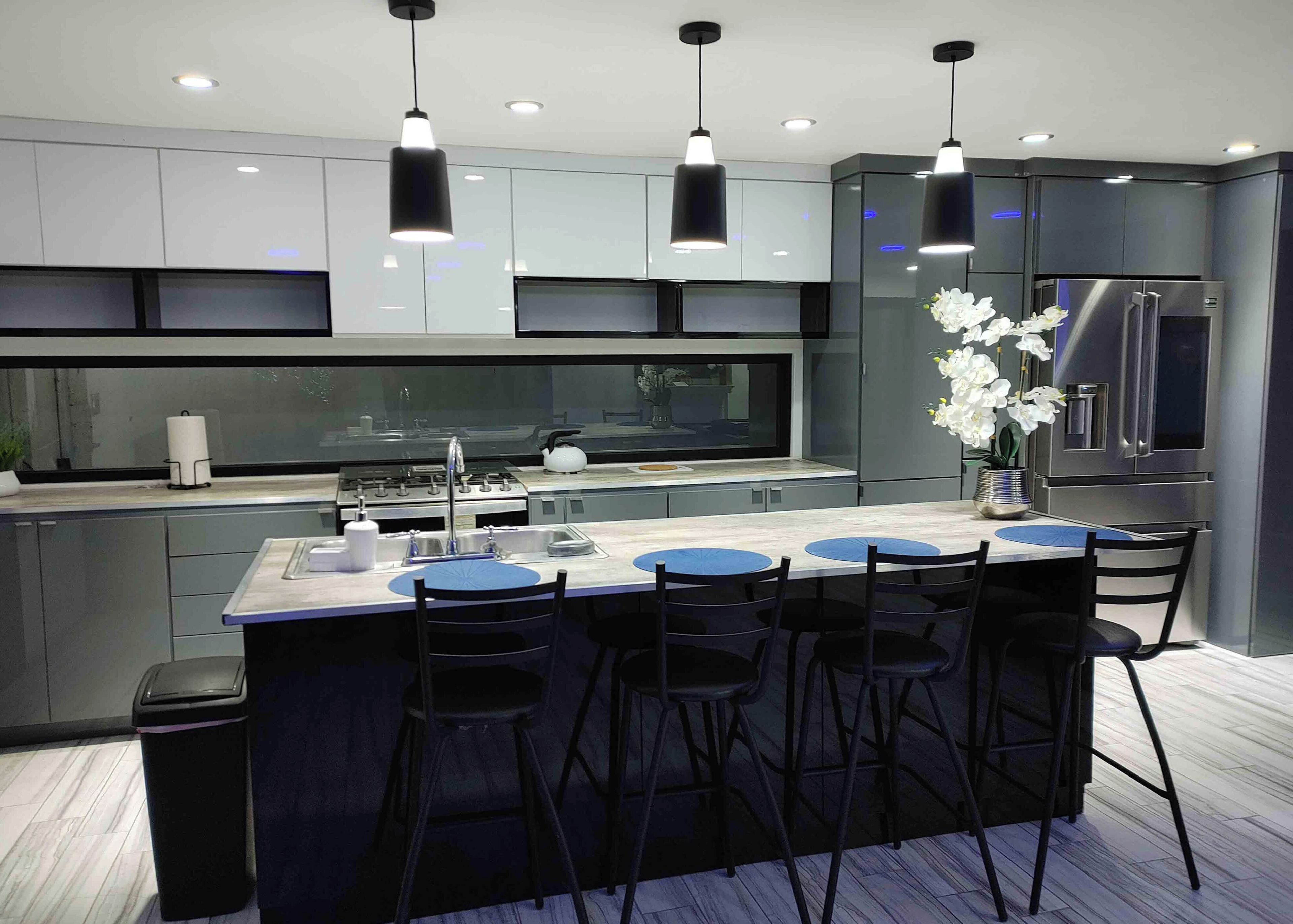 Una cocina moderna con una isla central, taburetes de bar y electrodomésticos de acero inoxidable.