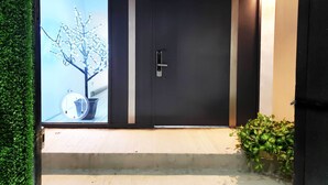 A modern entrance with a sliding glass door, a small outdoor seating area, and a potted plant. - Villas Beach House(next to the main Blvd. walking distance to the beach & A/C) (Rosarito)