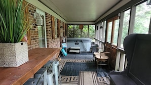 En overdækket terrasse med et træbord, metalstole, en bænk og en stor plantepotte.
