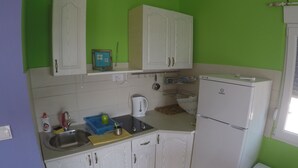 Una cocina compacta con armarios blancos, un lavamanos, un hervidor y un refrigerador.