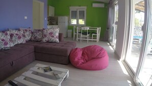 Una sala de estar con un sofá modular, un sillón de peluche, una mesa de centro y un comedor con sillas y una mesa.