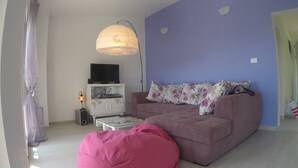 Una sala de estar con sofá, sillón de peluche, mesa de centro, televisor sobre un mueble bajo y lámpara.