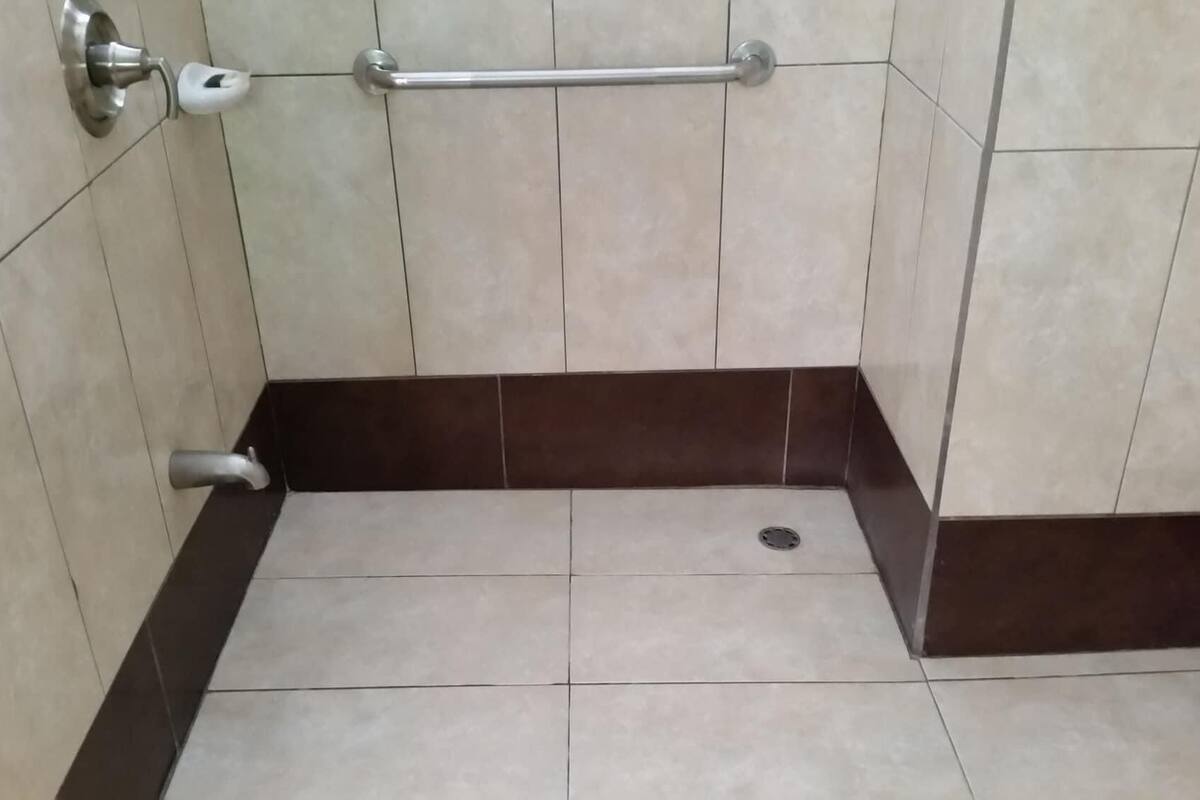 A bathroom with a handrail, a toilet, and a drain.