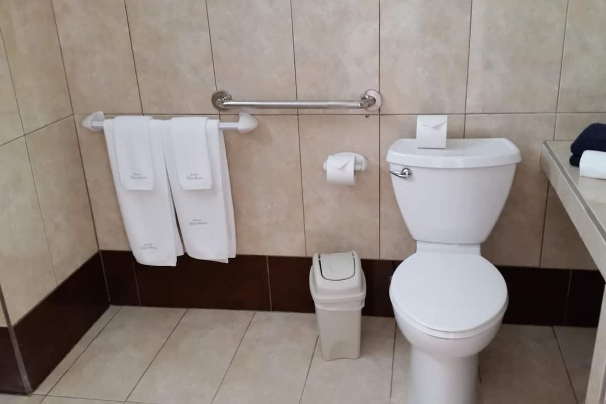 A bathroom with a toilet, a trash bin, a towel rack with towels, and a toilet paper holder.
