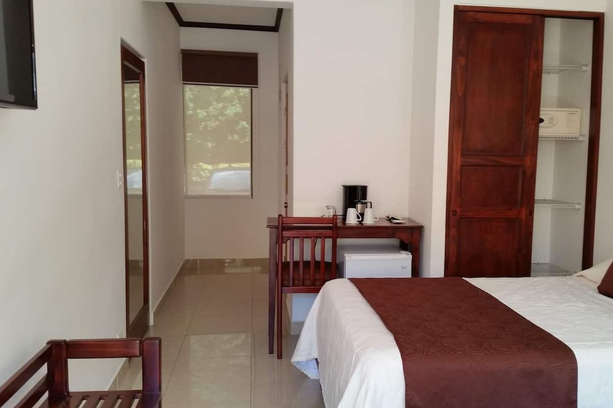 A hotel room with a bed, a desk with a chair, a wardrobe, and a window.