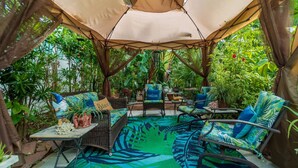 A covered outdoor seating area with wicker furniture and a tropical leaf-patterned rug.