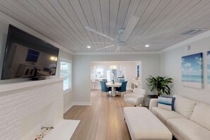 Un soggiorno moderno con una televisione a schermo piatto, una ventola a soffitto e un'area pranzo con sedie blu.