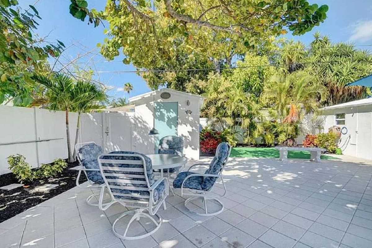 Un'area patio con tavolo e sedie, circondata da un recinto bianco e diverse piante.