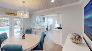 A modern kitchen with white cabinets, a central island, and a dining area with blue chairs and a round table. - The Lewis Properties (West Palm Beach)